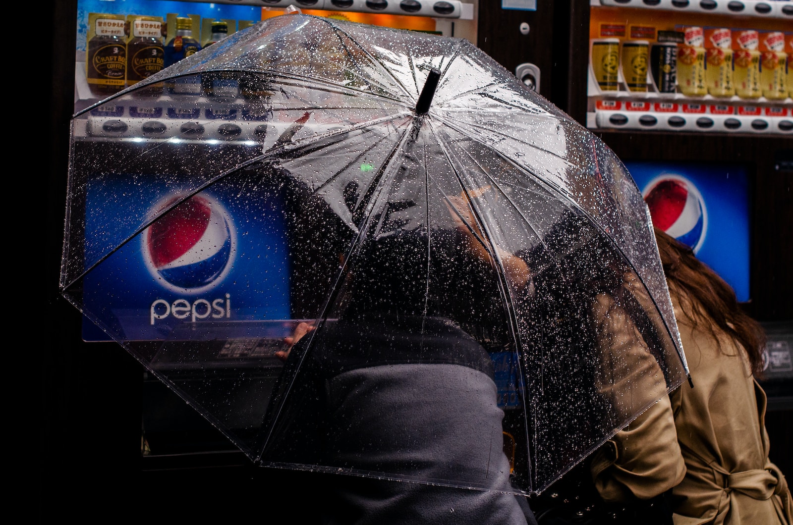 person under clear plastic umbrella near Pepsi vending machine